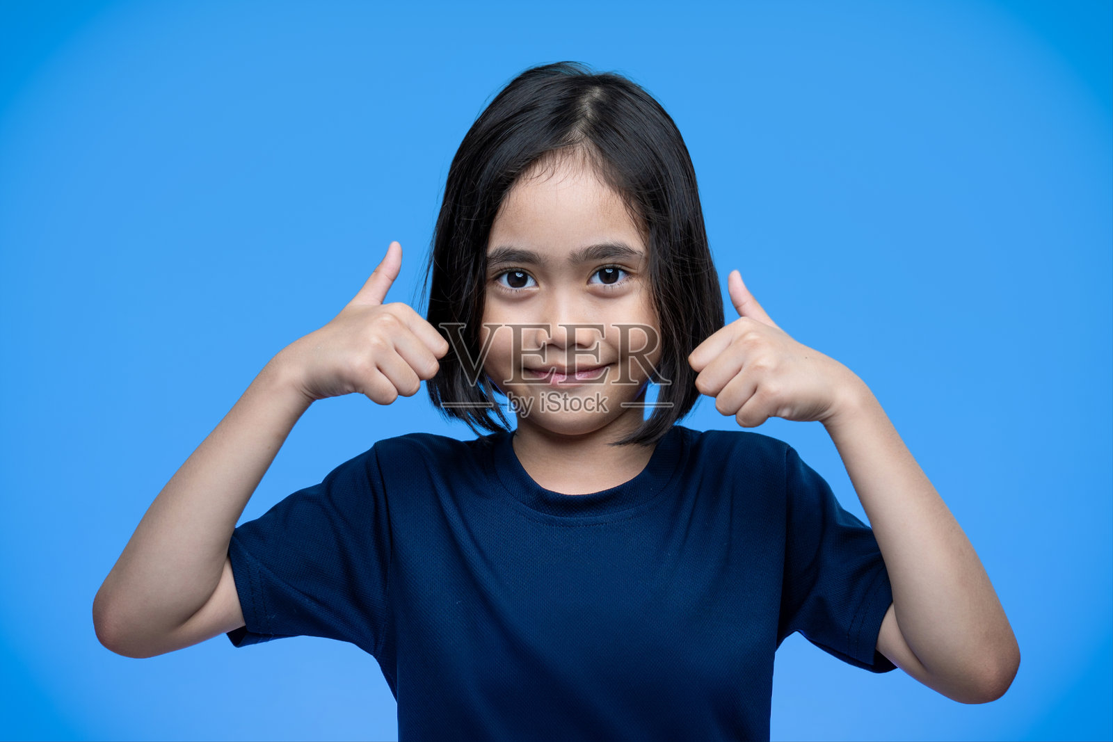 一个年轻的亚洲女孩微笑着，用双手做出竖起大拇指的手势。照片摄影图片