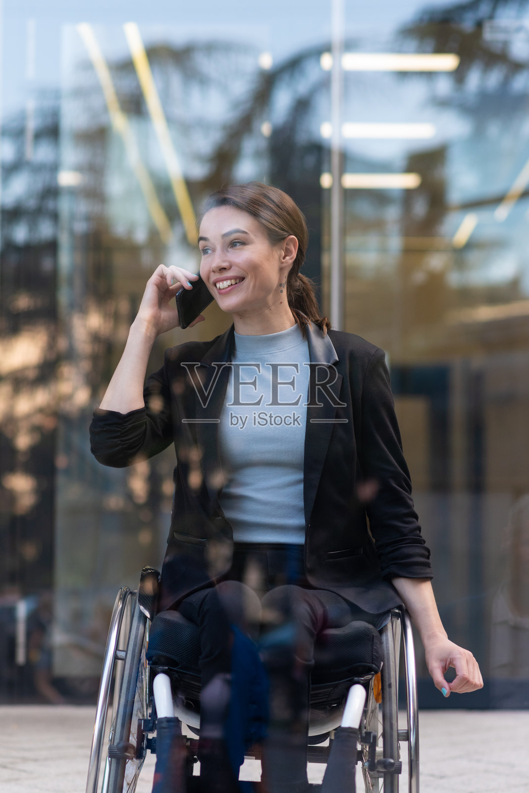 微笑的女商人在办公楼附近使用智能手机，坐在轮椅上照片摄影图片