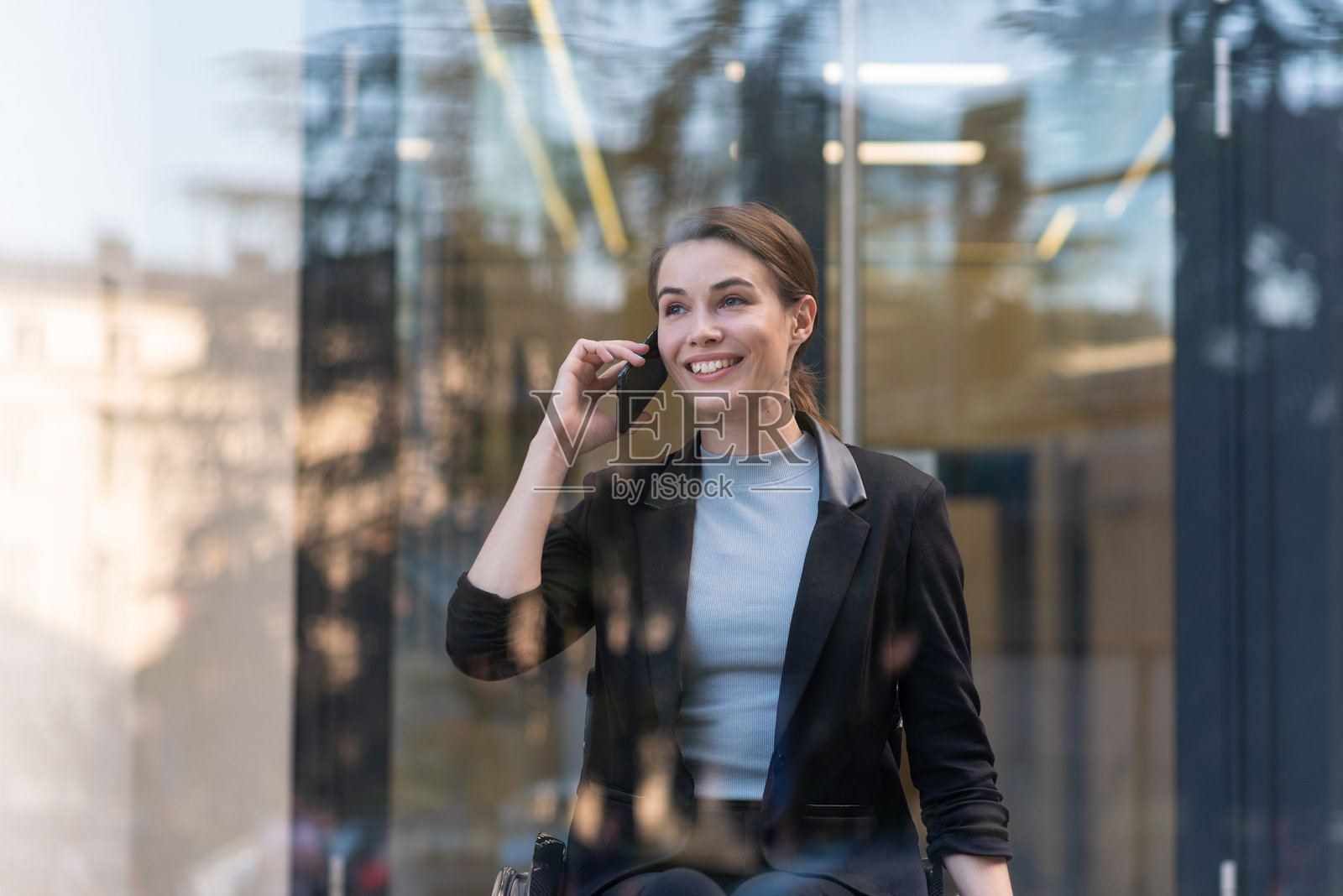 微笑的女商人在办公楼附近的轮椅上使用智能手机照片摄影图片