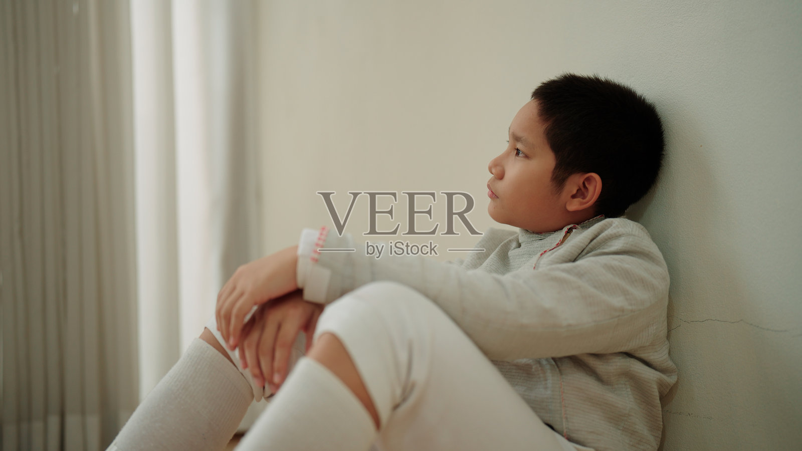 感到压力的年轻男孩安静地坐在地板上，双手托着头。照片摄影图片