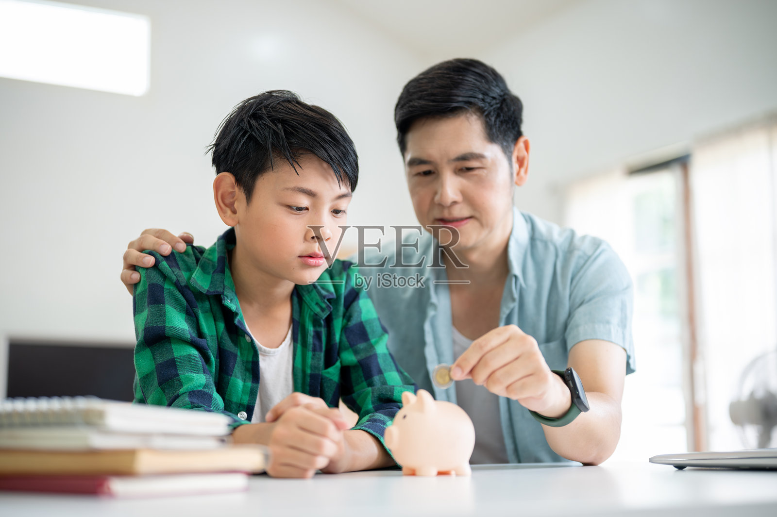 一个儿子专注地看着他的父亲把硬币放进粉色的储蓄罐里。存钱零花钱。照片摄影图片