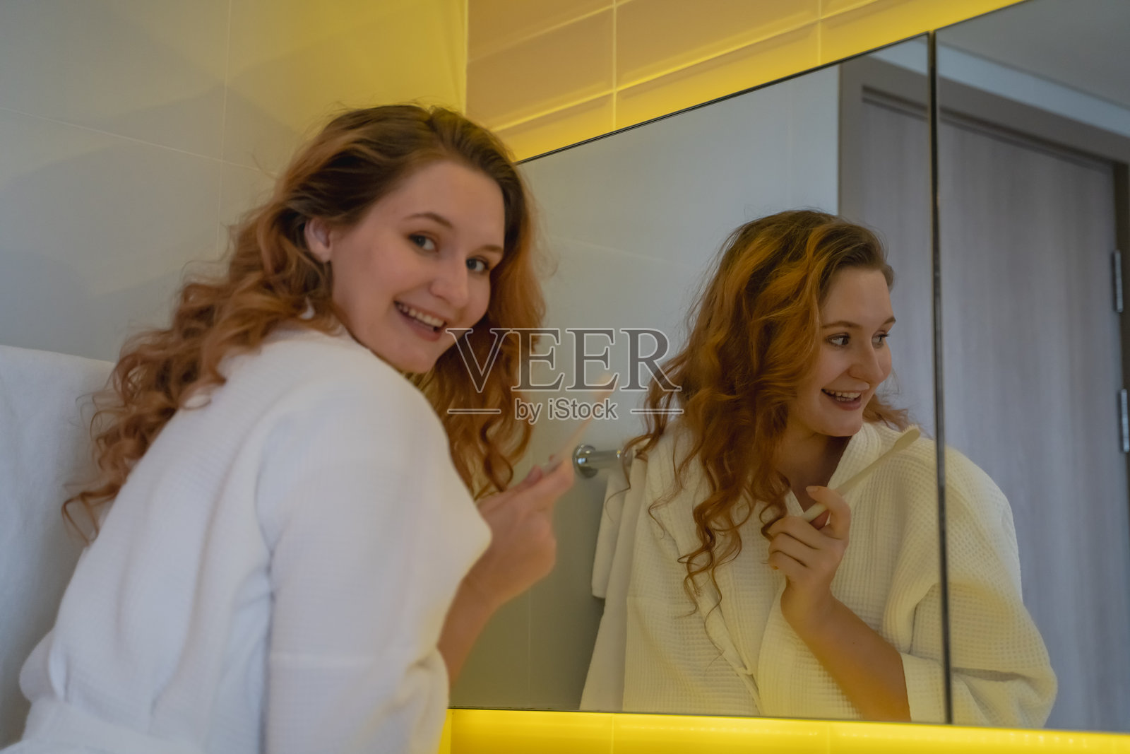 一位年轻女性早晨醒来后，站在浴室镜子前刷牙。照片摄影图片