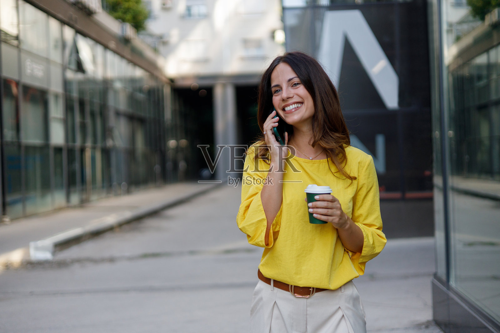 职业女性在城市街道上走着，一边打电话一边拿着外带咖啡。照片摄影图片