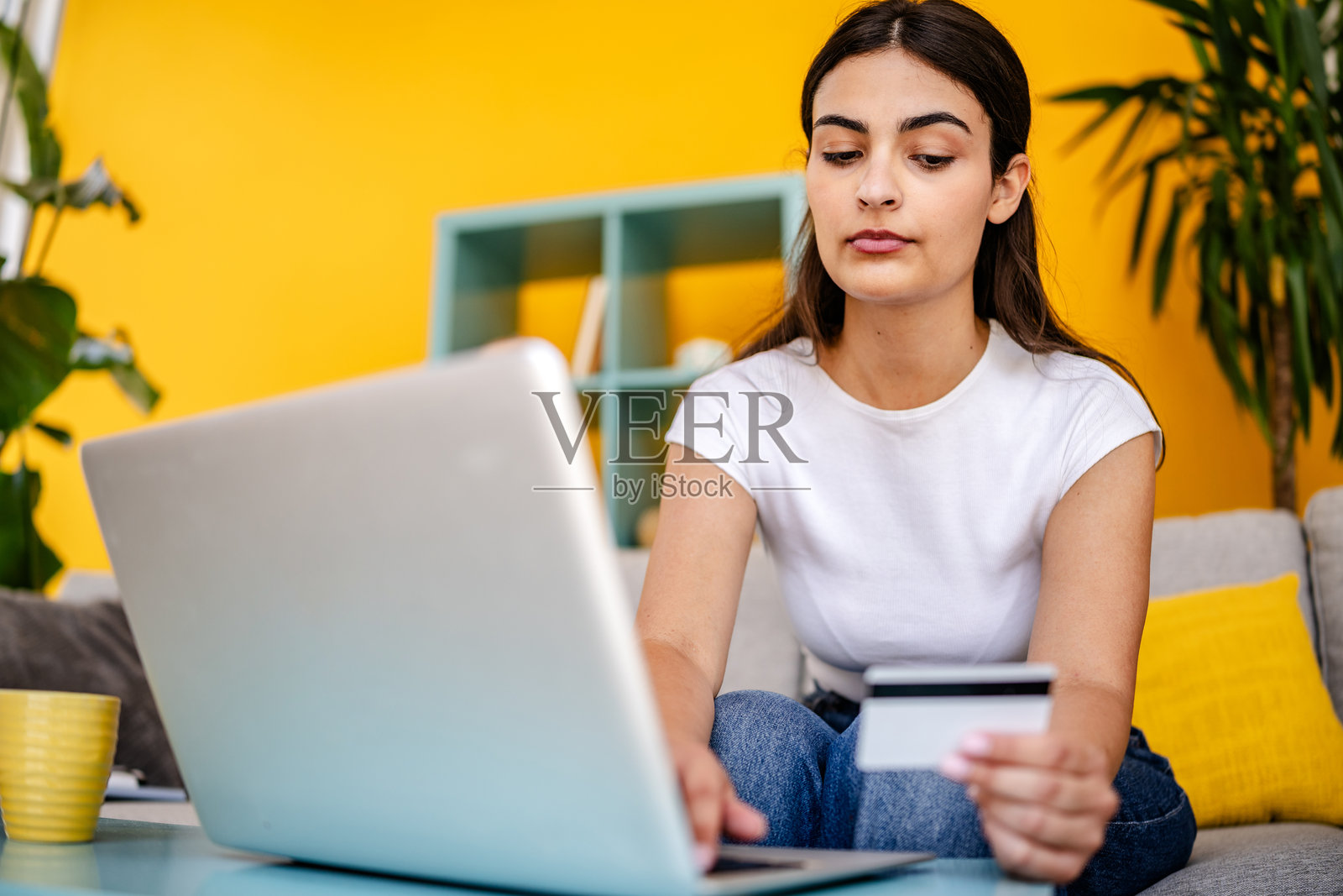 年轻女性在充满植物和黄色装饰的愉快客厅中进行在线购物照片摄影图片
