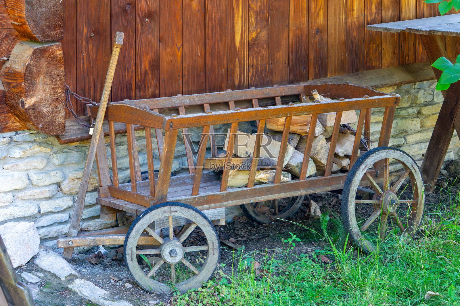 木制农场手推车，配有金属轮缘，靠在石基木谷仓的墙边。照片摄影图片