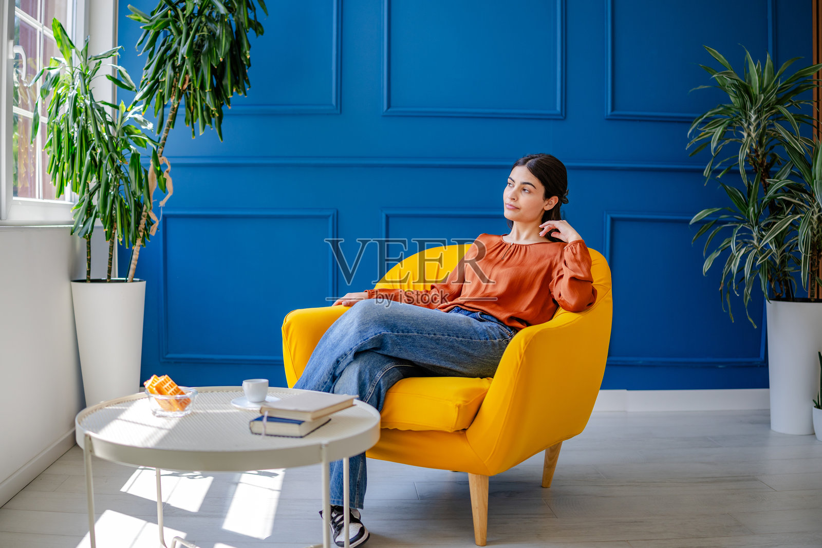 年轻女性在明亮的客厅中享受宁静时光，墙壁呈鲜艳的蓝色，家具舒适。照片摄影图片