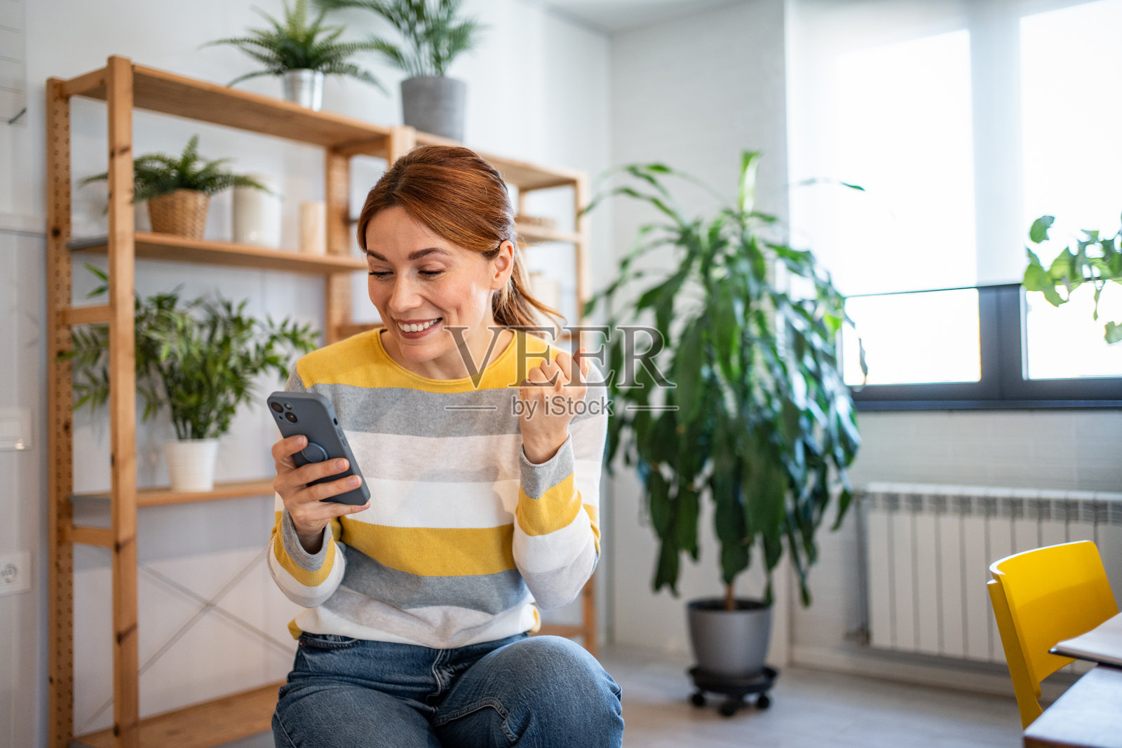 兴奋的女性在家中用智能手机庆祝成功照片摄影图片