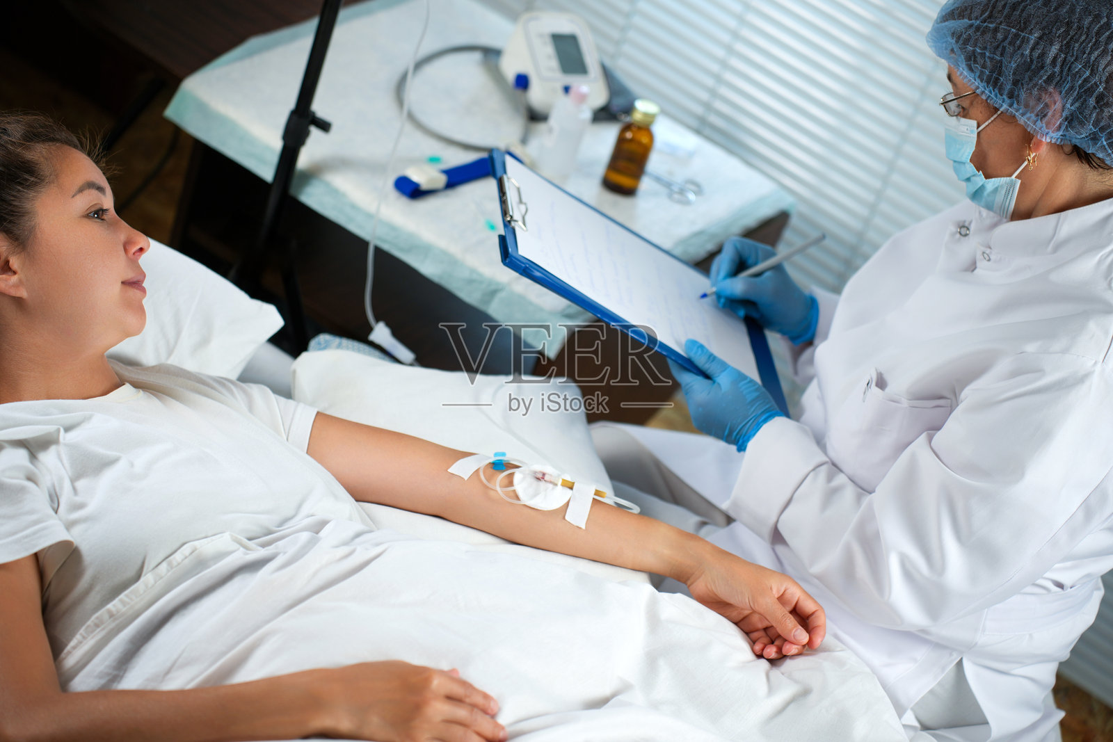 护士在监测一位接受静脉输液的年轻患者时做笔记照片摄影图片