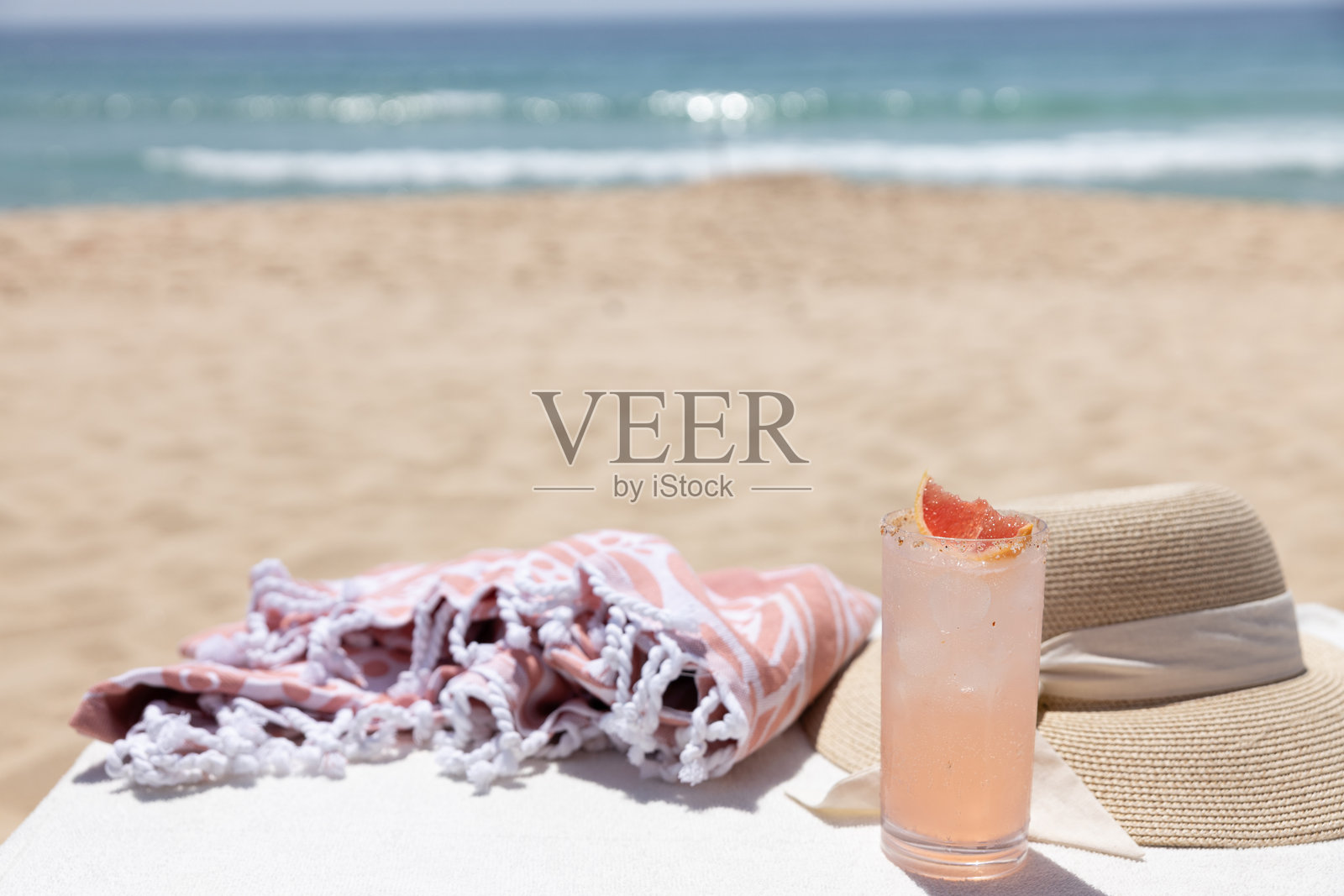 阳光明媚的海滩上有一杯鸡尾酒、一条毛巾和一顶帽子照片摄影图片