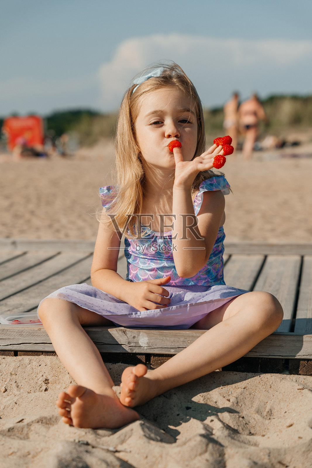 小女孩在温暖的阳光下享受零食，同时在海滩上玩耍照片摄影图片