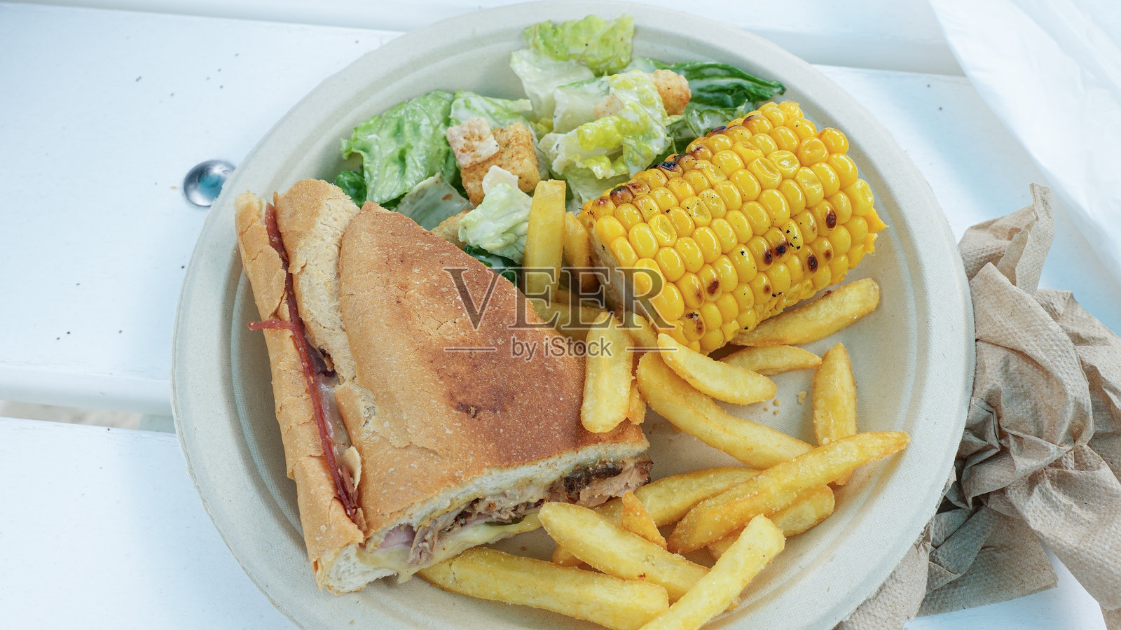 美味的三明治配上酥脆的薯条、新鲜的沙拉和烤玉米，展示出色彩鲜艳、令人垂涎的餐点呈现。照片摄影图片