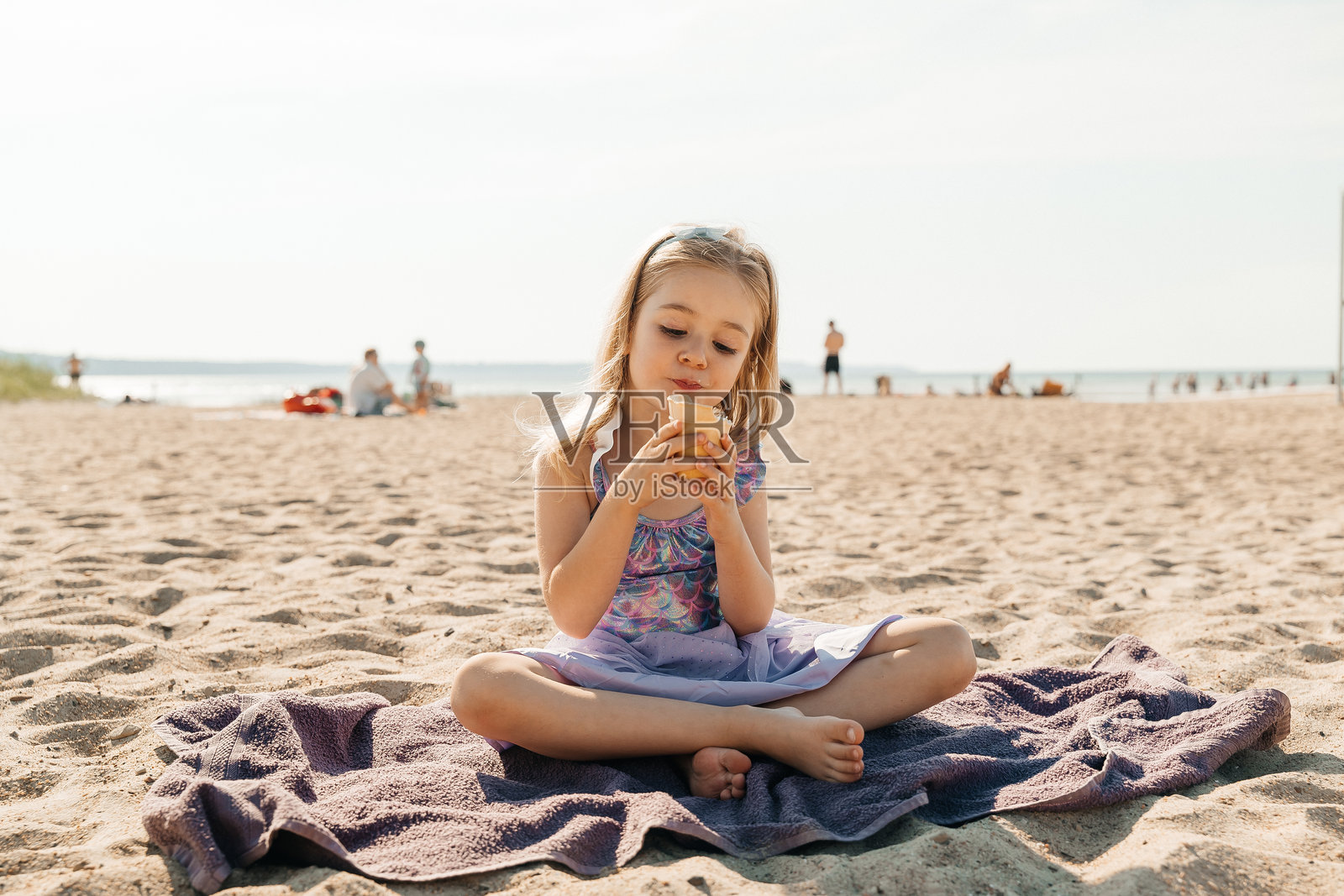 小女孩在阳光明媚的日子里坐在海滩上享受冰淇淋照片摄影图片