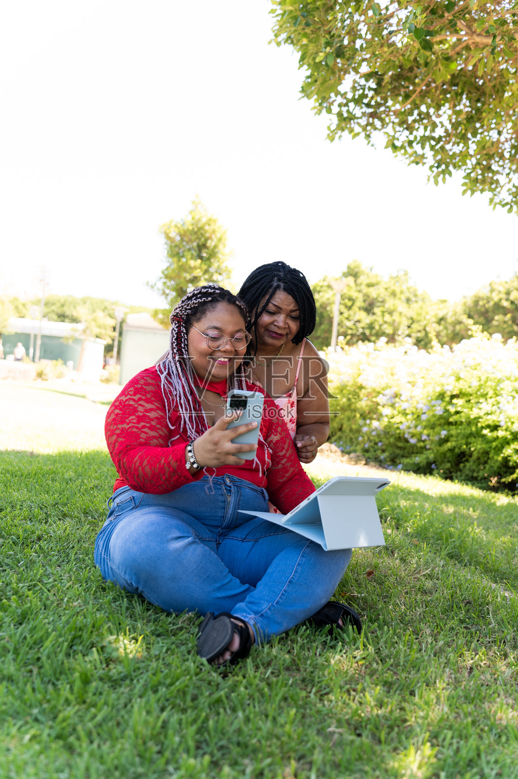 母亲和女儿在公园里使用智能手机和平板电脑照片摄影图片