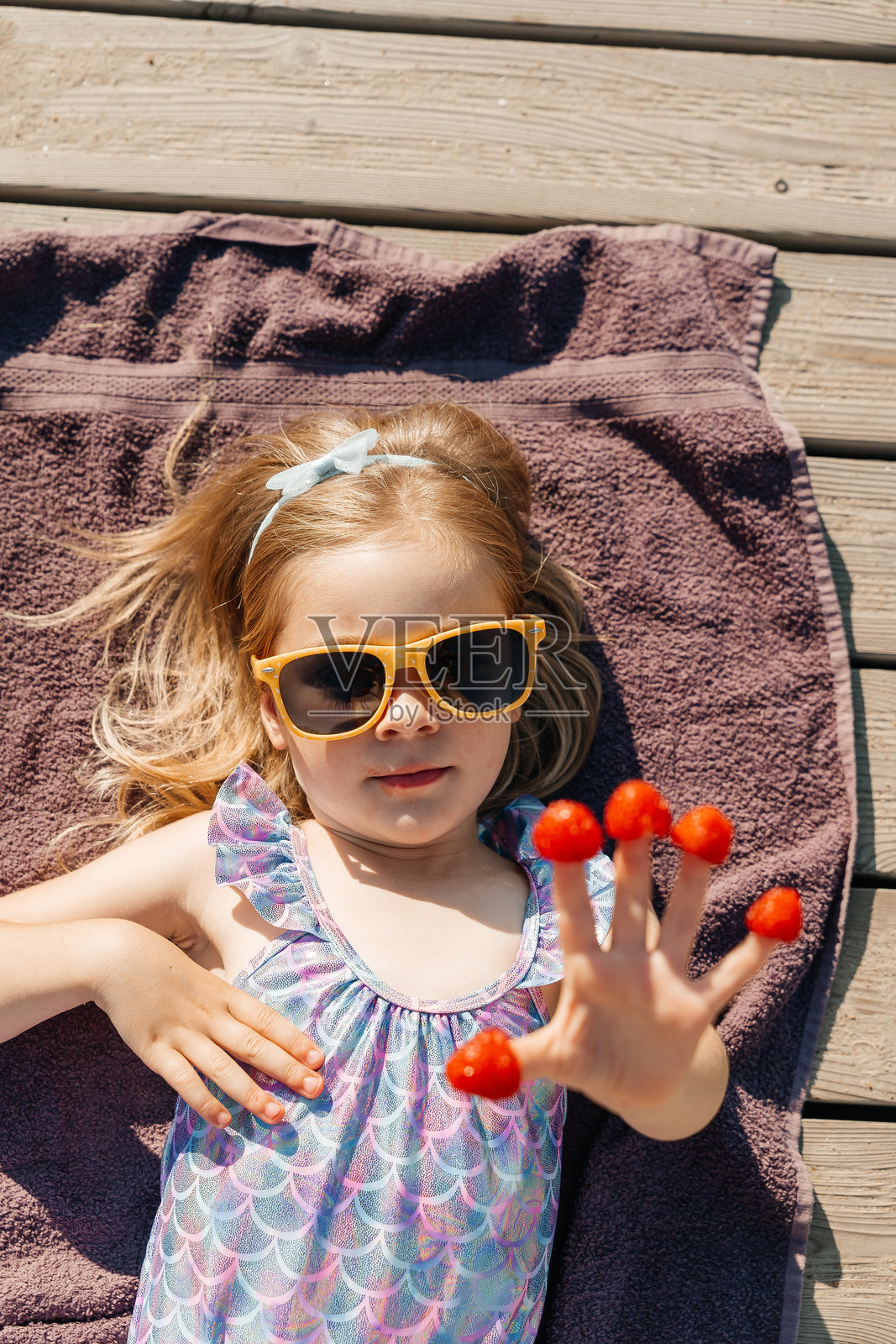 孩子在阳光明媚的日子里，戴着太阳镜，手指上沾着覆盆子，悠闲地享受户外时光。照片摄影图片