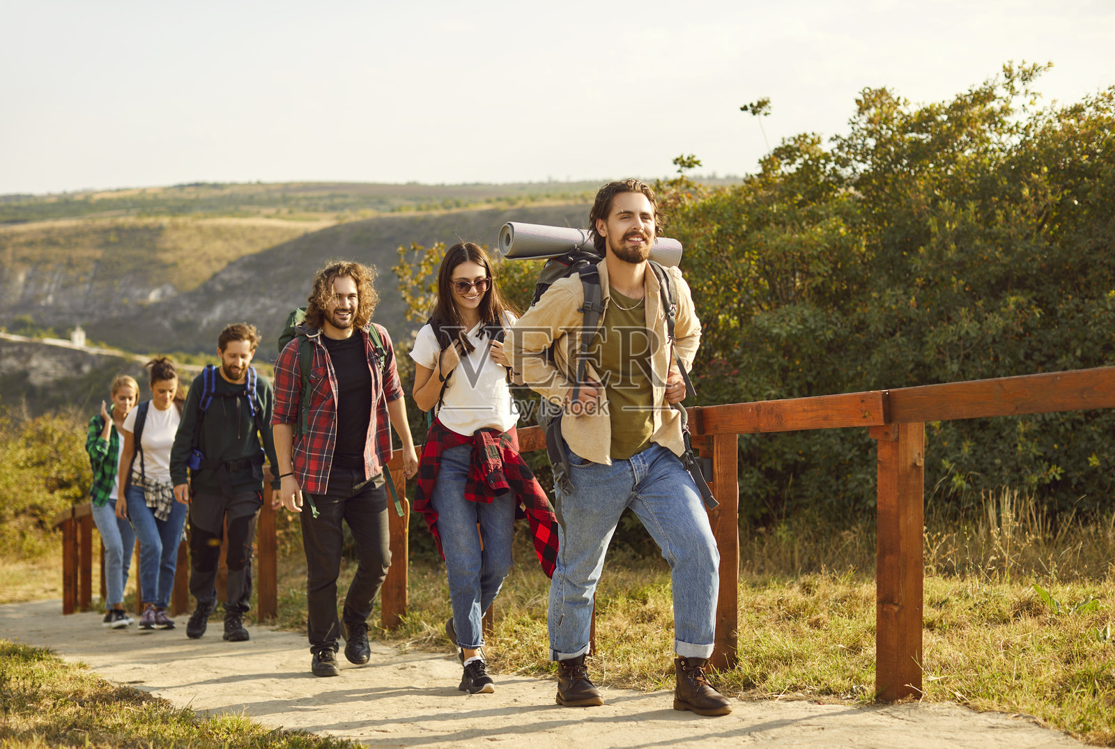 一群男女徒步旅行者背着大背包在大自然中排成一行行走。照片摄影图片