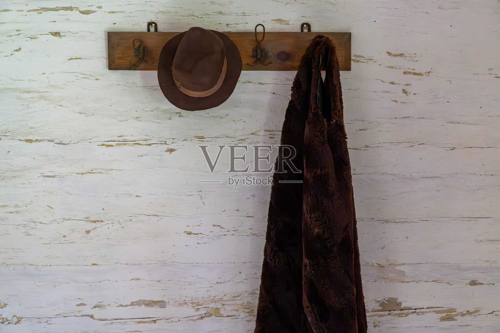 白色磨损墙面上挂着一顶帽子和棕色外套的木质墙挂架照片摄影图片