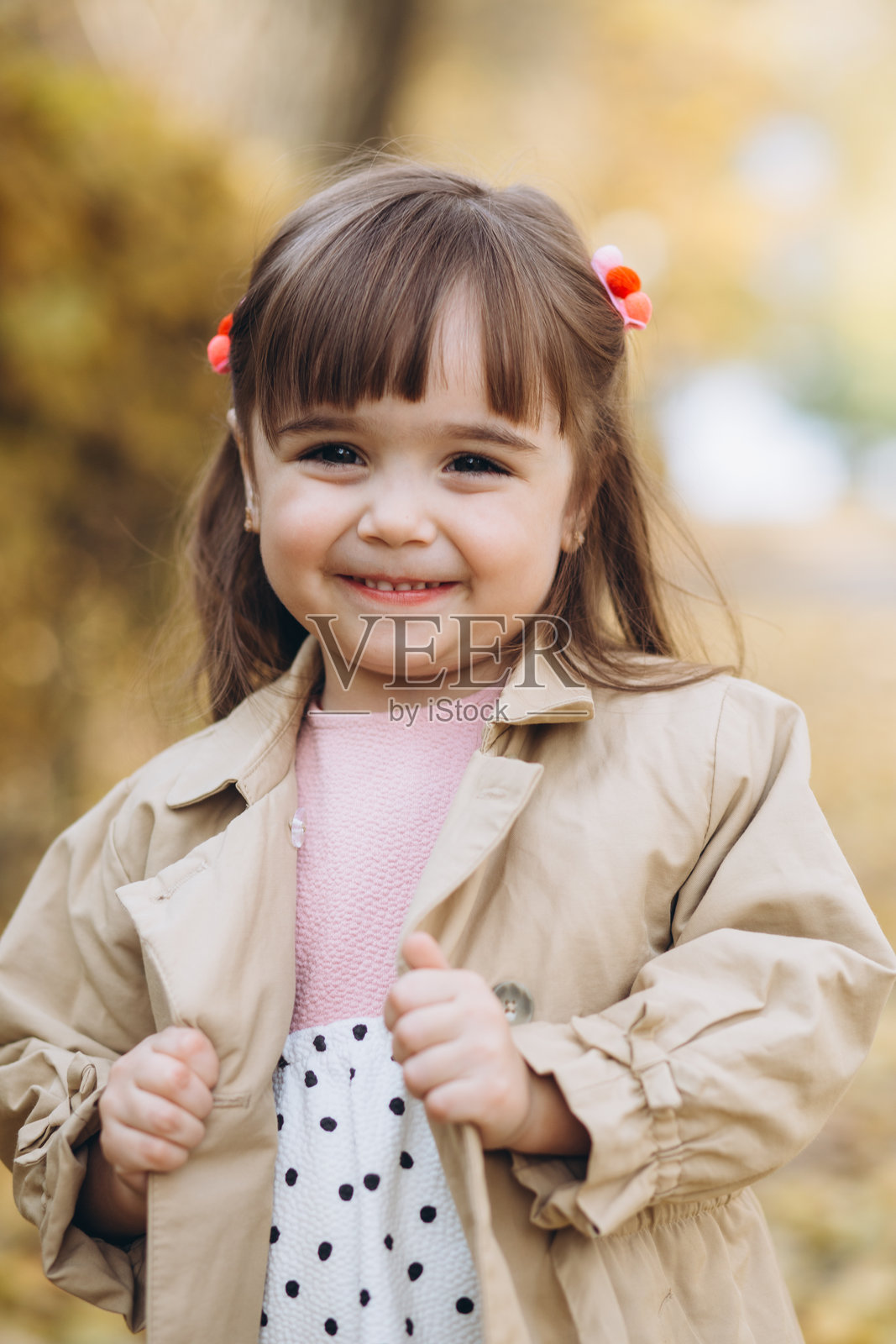 快乐而美丽的小女孩穿着米色外套在秋天的公园里散步照片摄影图片