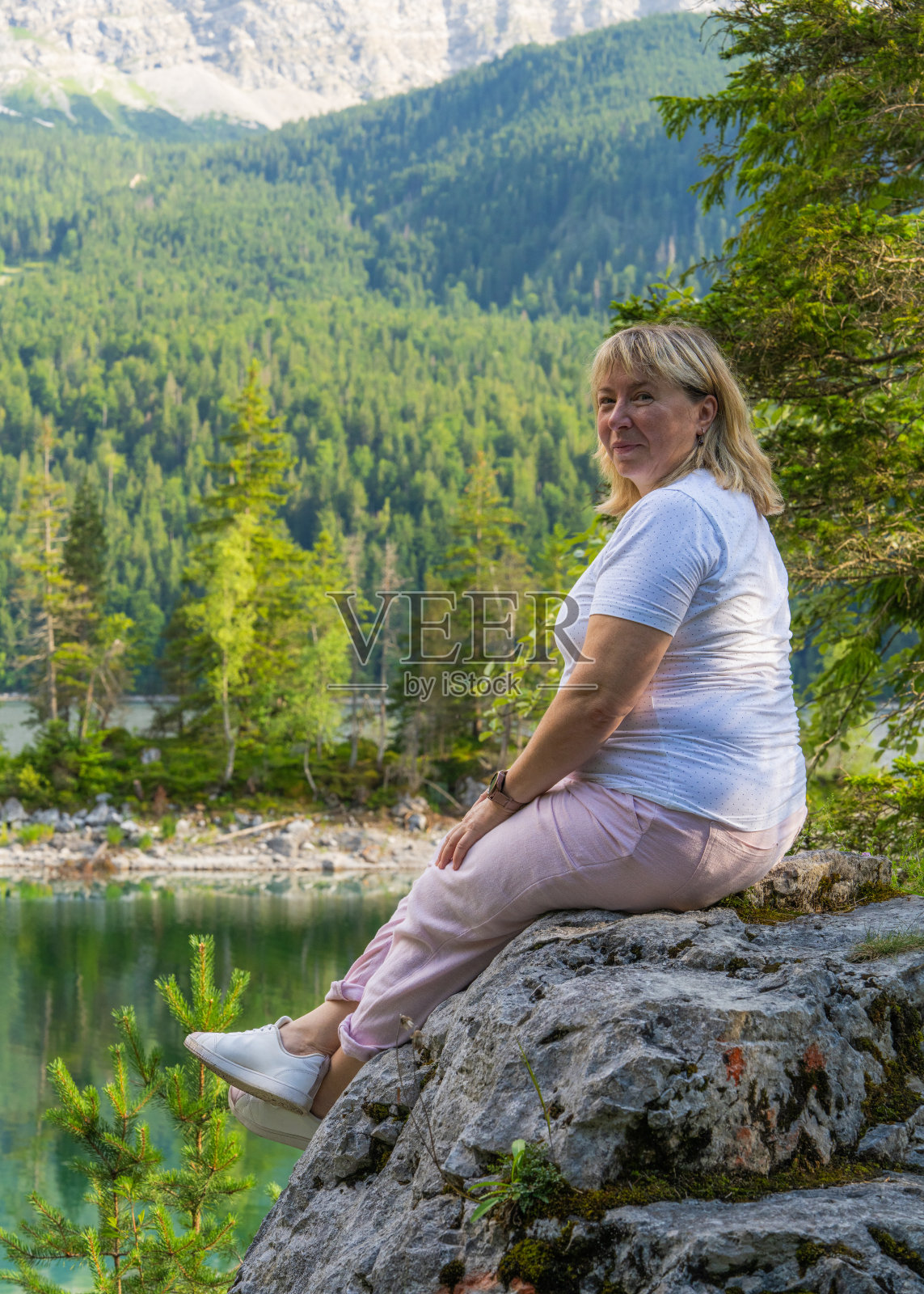 中年女性坐在岩石上，欣赏德国楚格峰附近艾布湖和巴伐利亚阿尔卑斯山的美丽景色。宁静的高山风光，非常适合旅行和徒步旅行。照片摄影图片