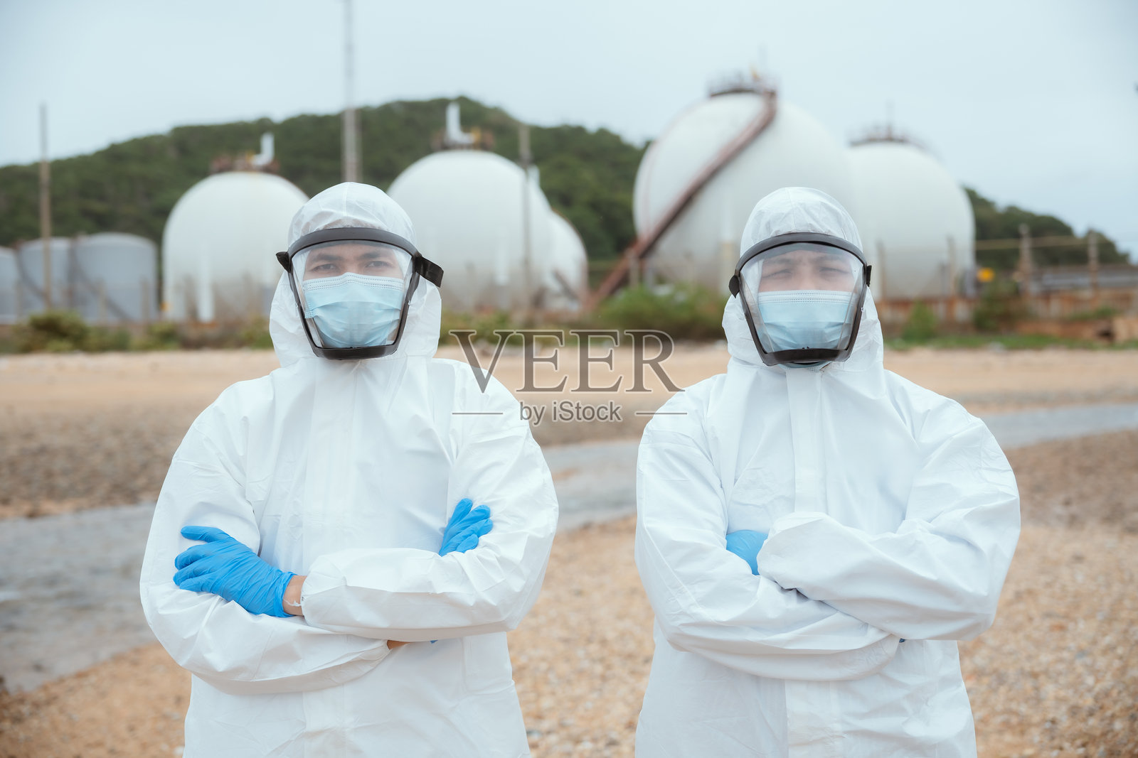 科学家们穿着防护服在一个平静的环境中，在阴天的海岸场地附近的储罐旁进行研究照片摄影图片