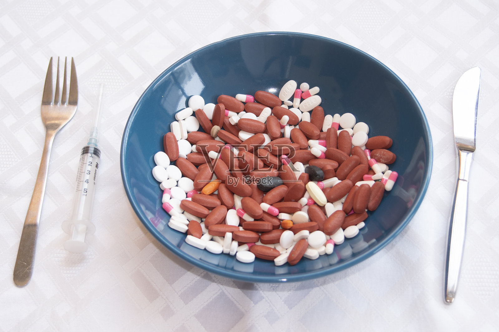 白色桌布上的药丸、注射器、叉子和刀。健康与时间的概念。照片摄影图片