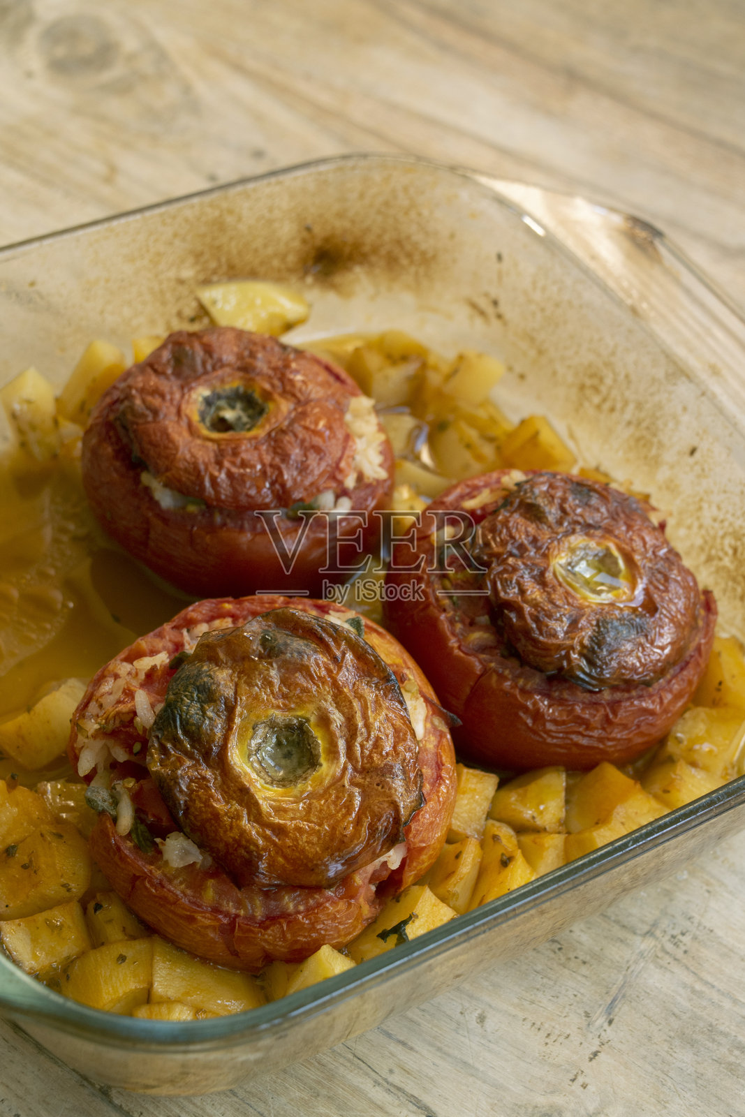 烤制的米饭和香草填充番茄，放在玻璃盘中，配以土豆。照片摄影图片