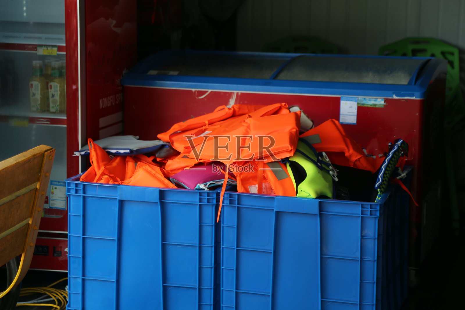 一个装满救生衣和其他安全设备的蓝色塑料箱放在冰淇淋店的开门旁边。照片摄影图片