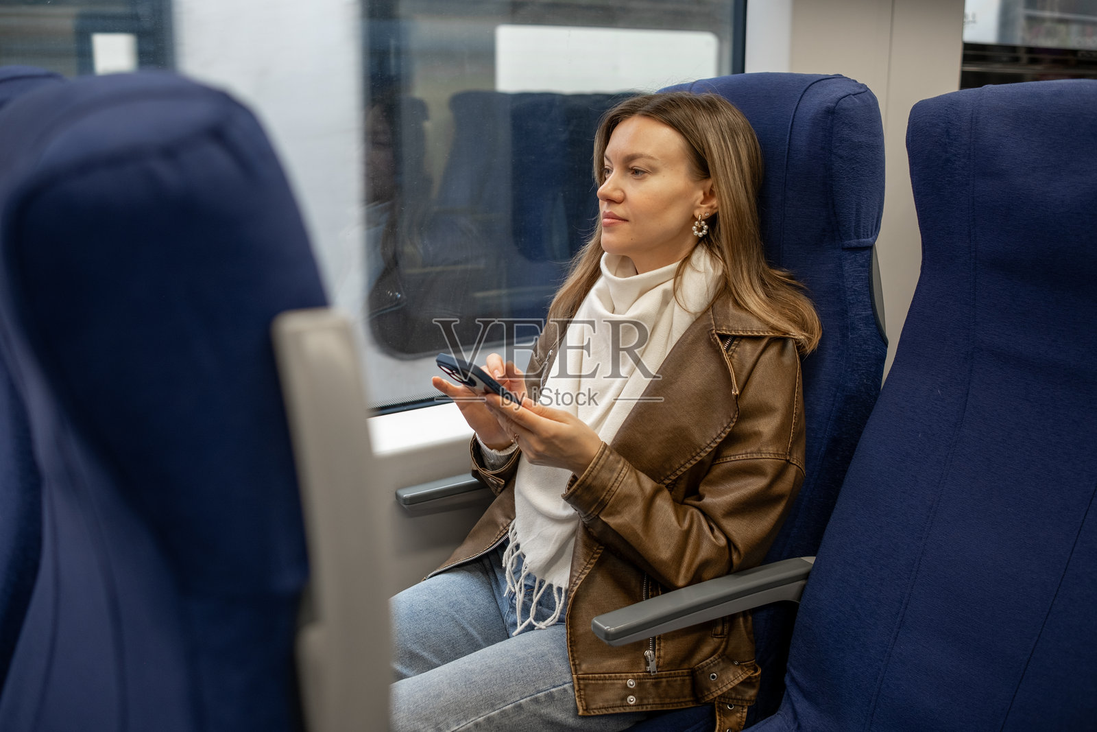 穿着舒适服装的女性在白天的火车上坐着使用智能手机照片摄影图片