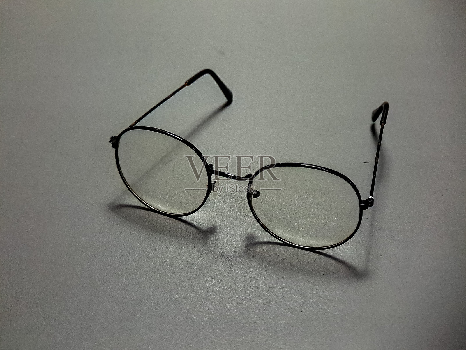 眼镜静静地放置在一个简单的工作室场景中，形成了一种有趣的光学工具展示，具有复古的美学和设计，背景和表面为灰色。照片摄影图片