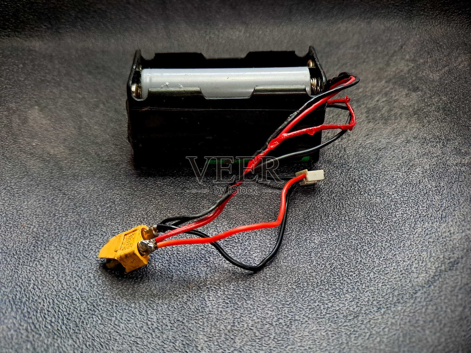 一个电池组，带有红色和黑色电线连接到一个黄色连接器，放置在一个有纹理的灰色表面上，展示电力和连接的电气组件。照片摄影图片