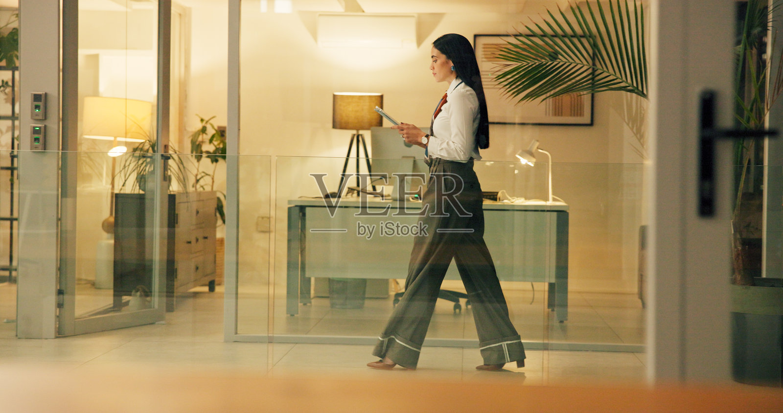 商务女性在夜晚使用平板电脑，连接互联网，进行文案写作和应用开发。傍晚，现代办公室中的人和记者，进行沟通和研究以撰写文章并走动。照片摄影图片