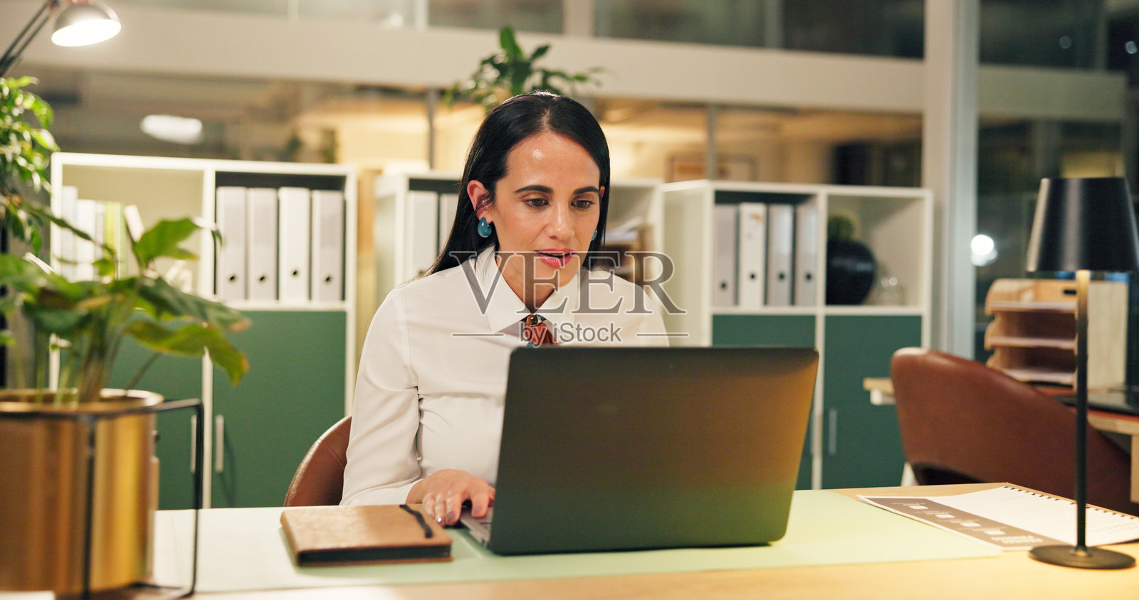 商务、夜晚和女性在工作场所，使用笔记本电脑在线阅读电子邮件、投资和经济。晚上，金融顾问在办公室，使用电脑和互联网进行股票市场和交易。照片摄影图片