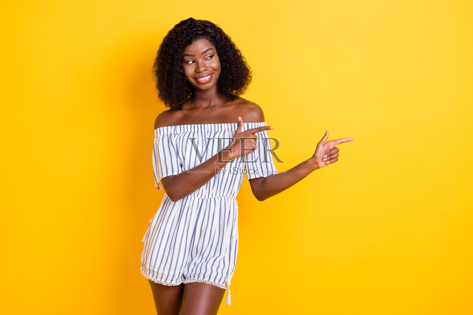 可爱的深肤色女性穿着条纹服装，指向空旷的地方，背景为黄色。照片摄影图片