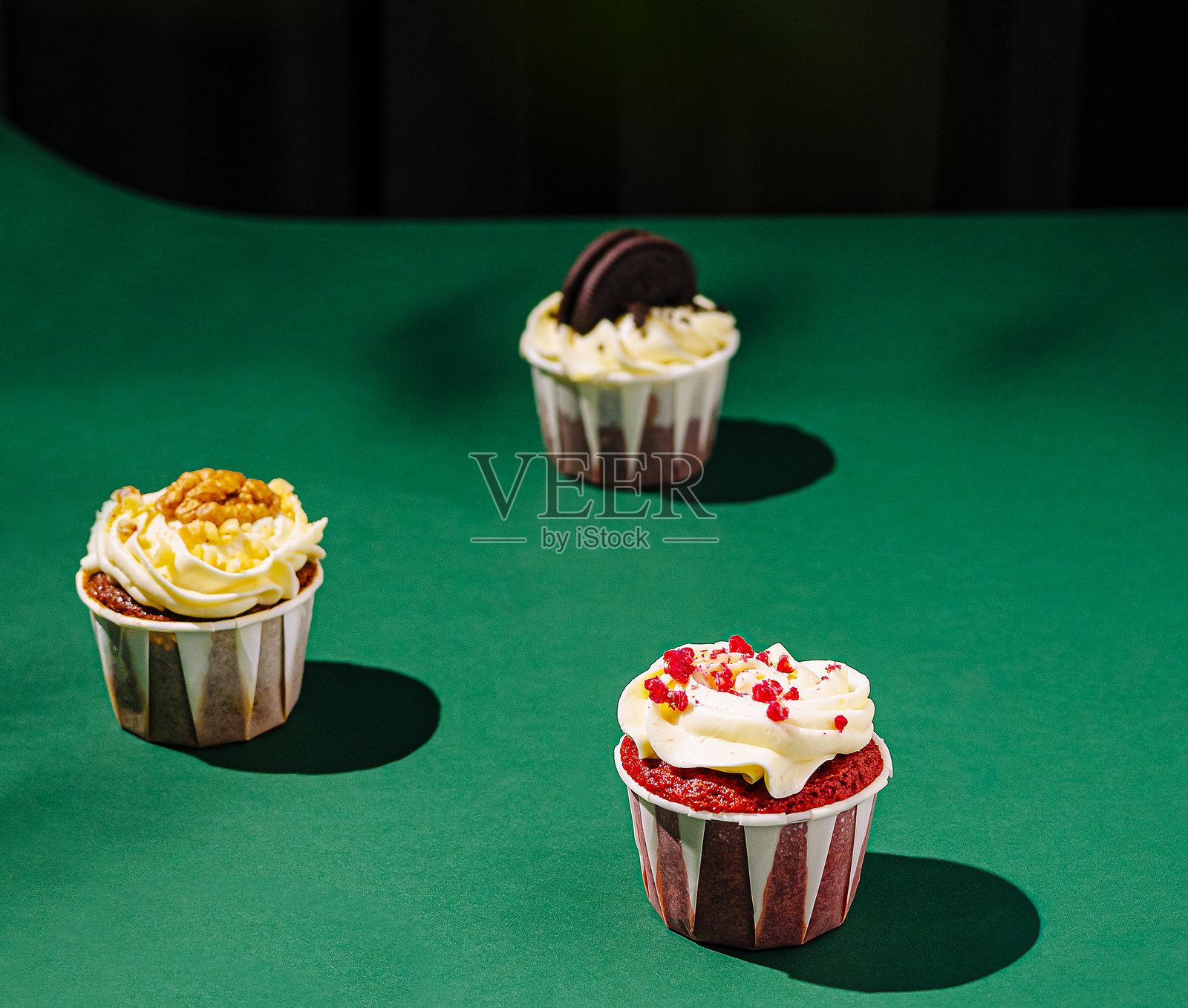 五颜六色的杯子蛋糕在明亮的灯光下排列在绿色表面上照片摄影图片