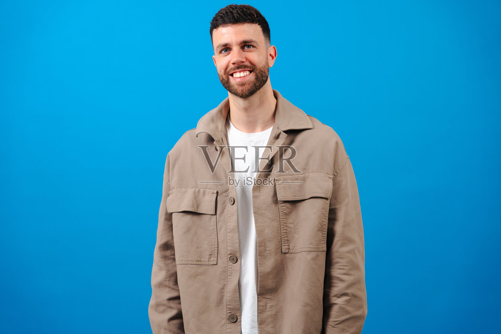 微笑的男子穿着休闲的米色夹克，站在蓝色背景前照片摄影图片