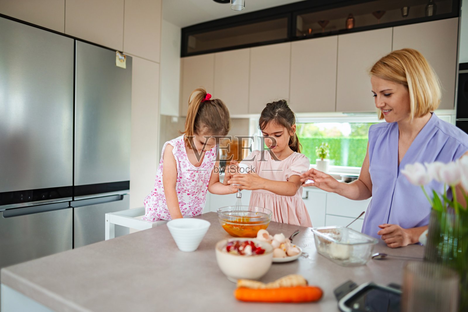 母亲和女儿们在厨房里打蛋。照片摄影图片
