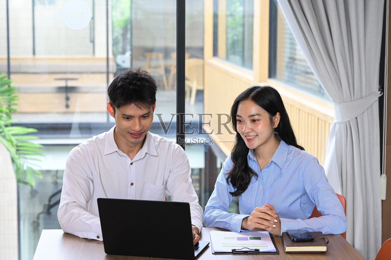 两位同事在现代工作空间中使用笔记本电脑合作进行商业项目。照片摄影图片