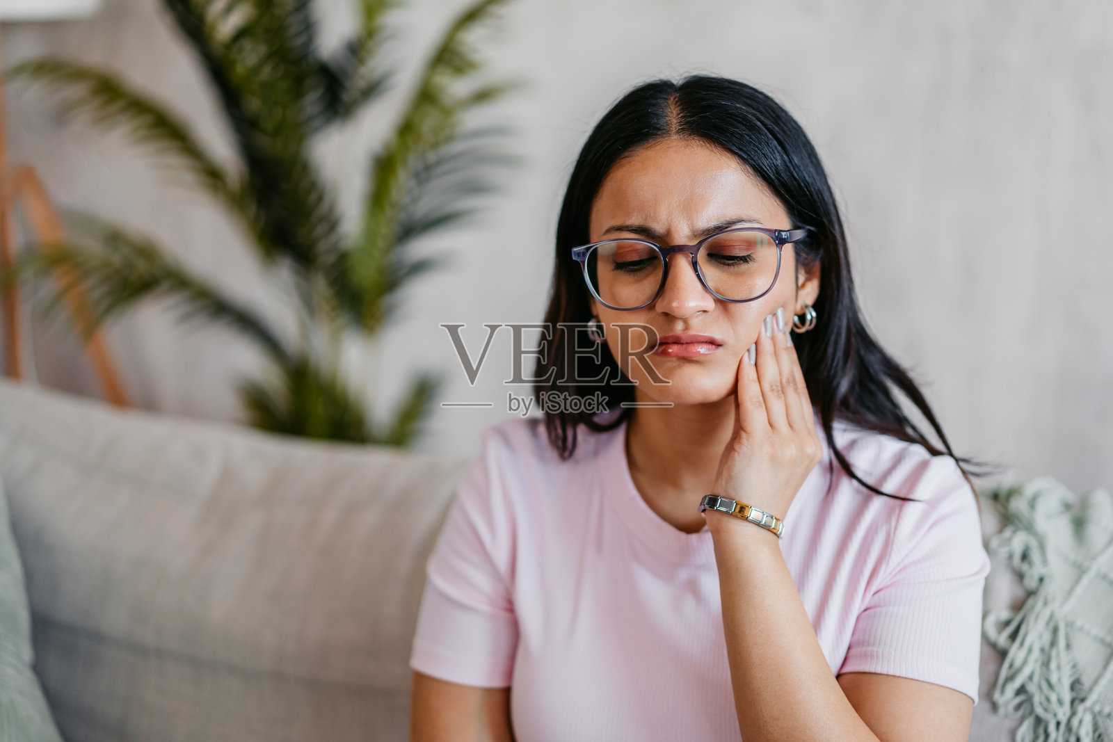 年轻印度女性坐在家里的沙发上，牙痛。照片摄影图片