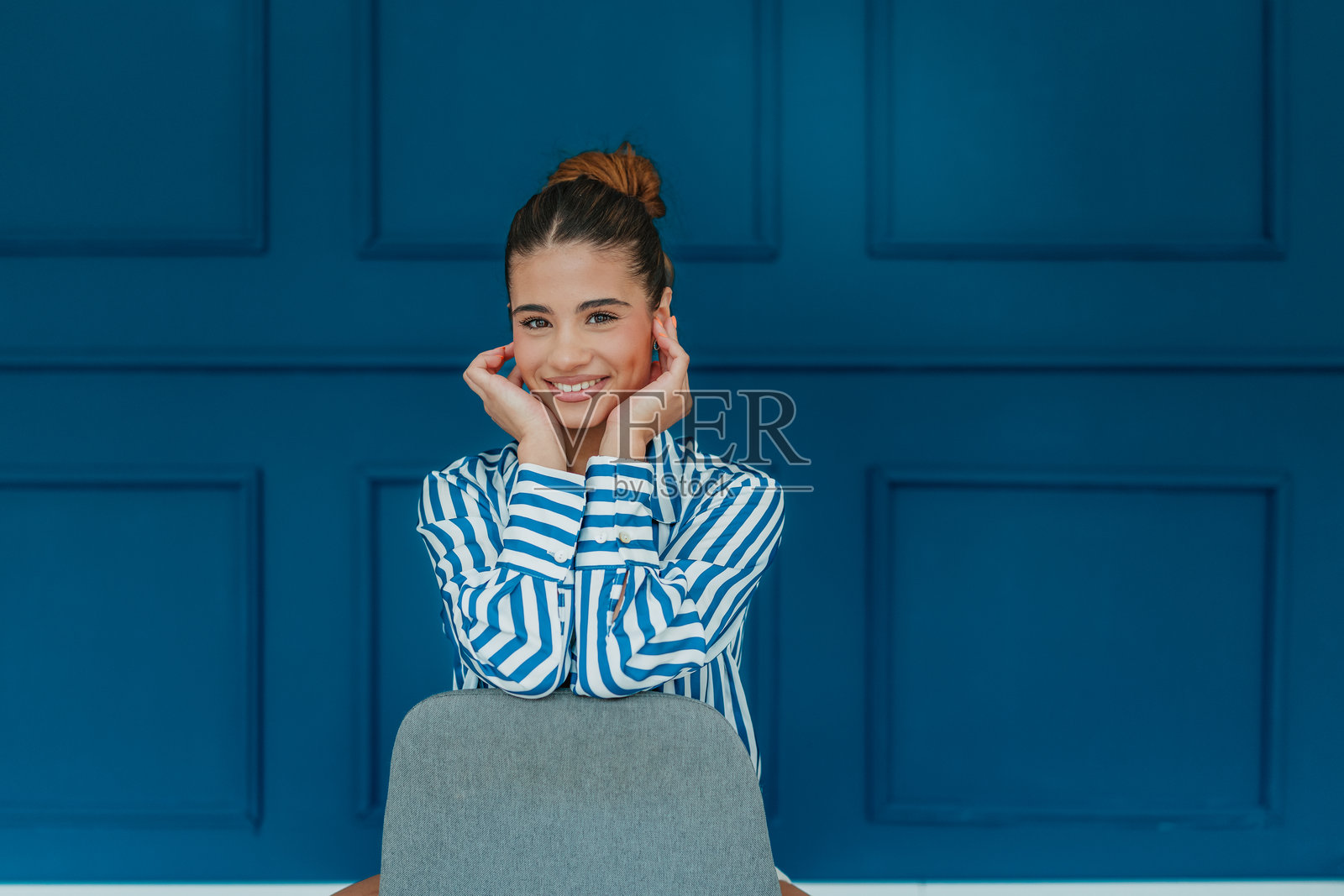 年轻女性在现代客厅中微笑，蓝色墙壁和时尚装饰，白天的场景照片摄影图片