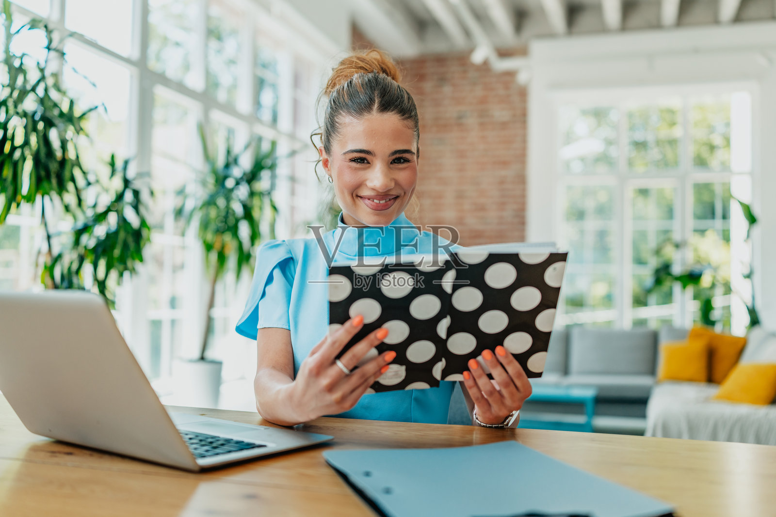 年轻女性在明亮的客厅中微笑着阅读一本书，周围有自然光和室内植物。照片摄影图片