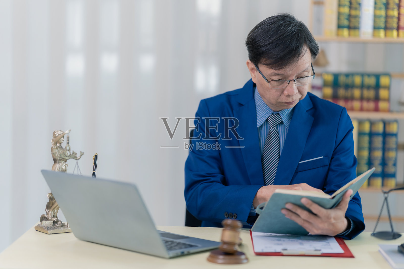 一位穿着笔挺西装的律师或会计师坐在桌前，使用笔记本电脑查看案件文件。照片摄影图片