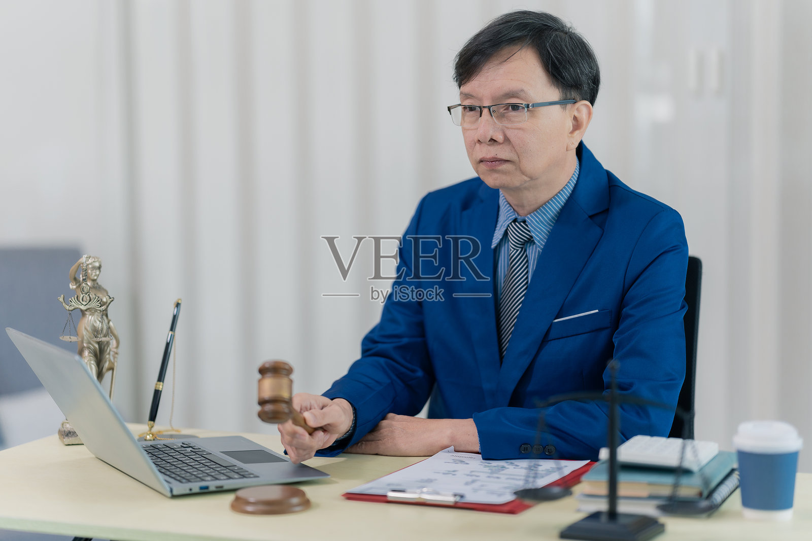 一位身穿笔挺西装的律师或会计师正在桌前使用笔记本电脑，审阅案件文件。照片摄影图片