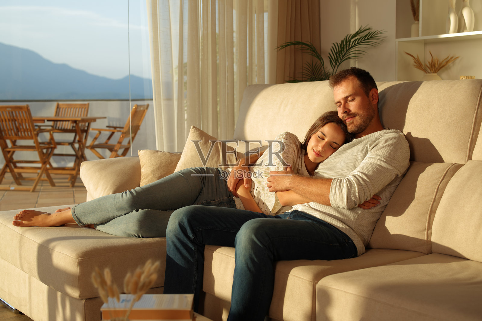 在家中，情侣在日落时分依偎在沙发上休息。照片摄影图片