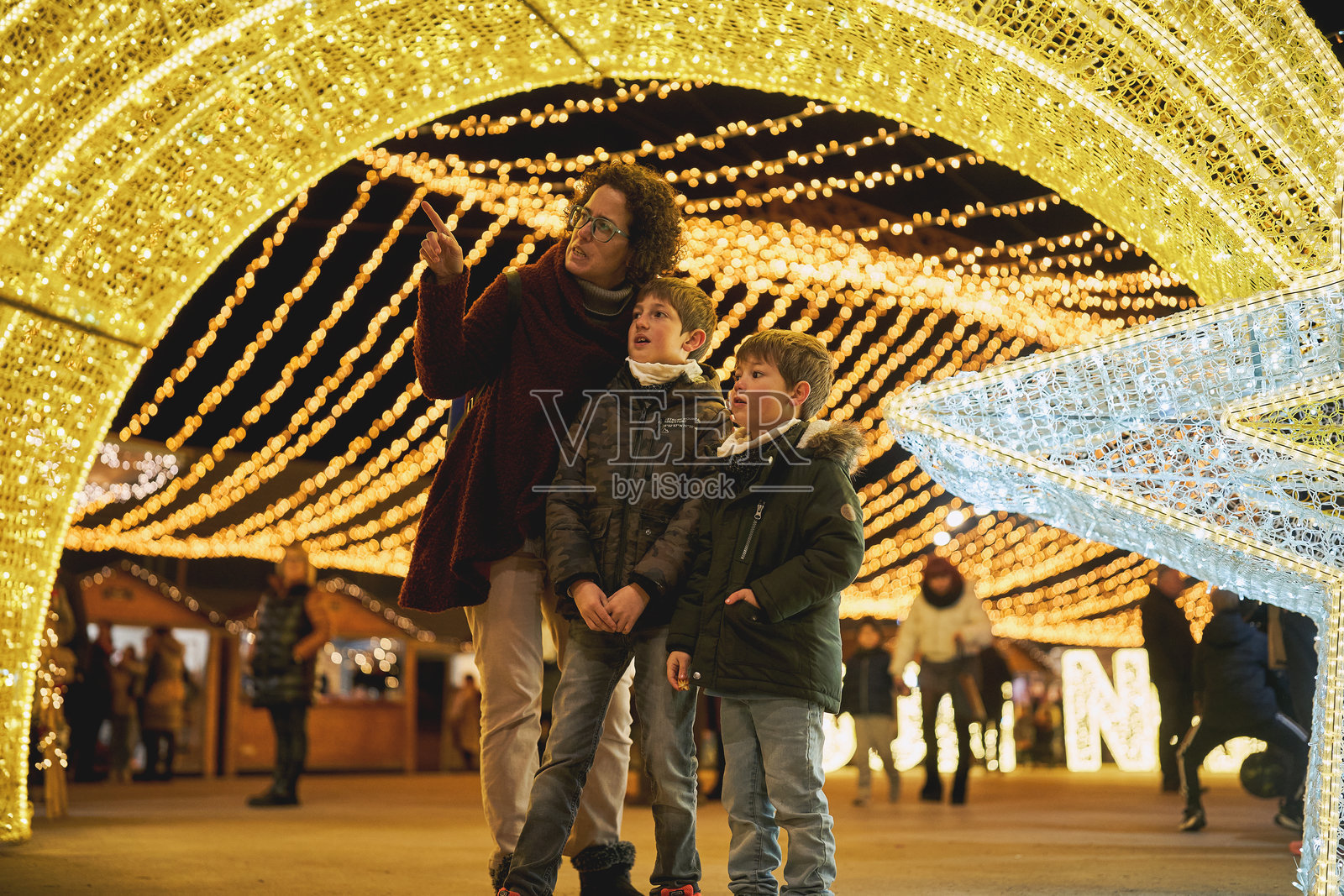 母亲在节日夜市上指给两个儿子看圣诞灯饰照片摄影图片