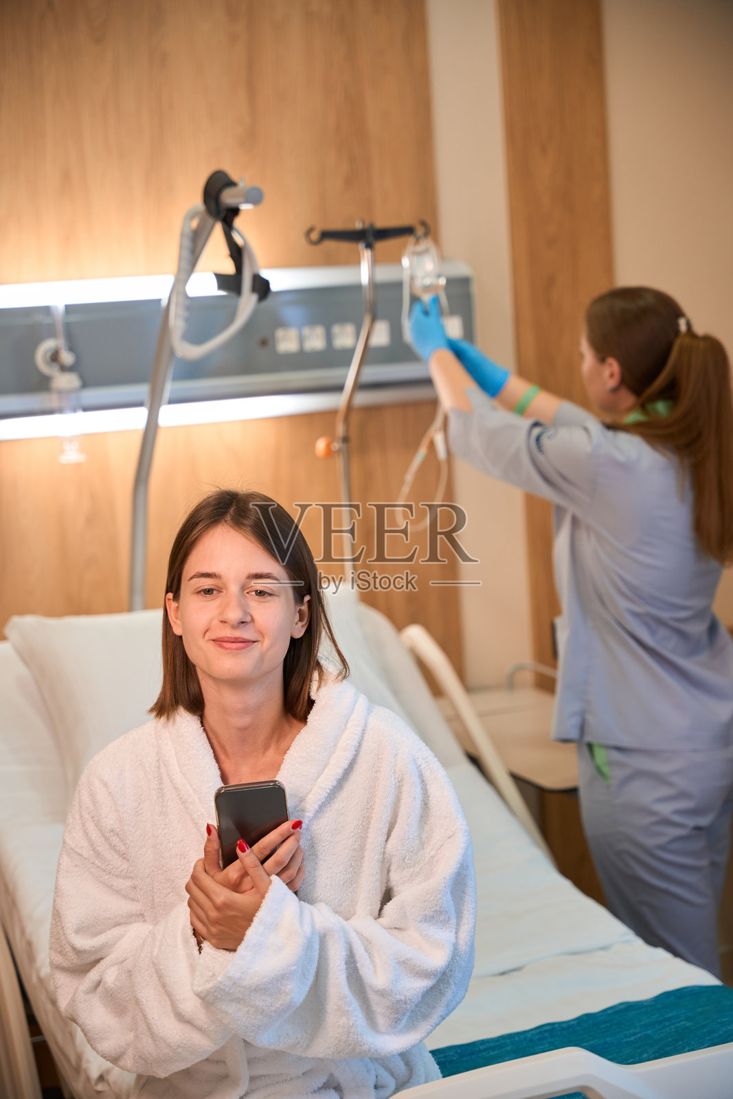 穿着医院病服的年轻女性在治疗期间查看智能手机照片摄影图片