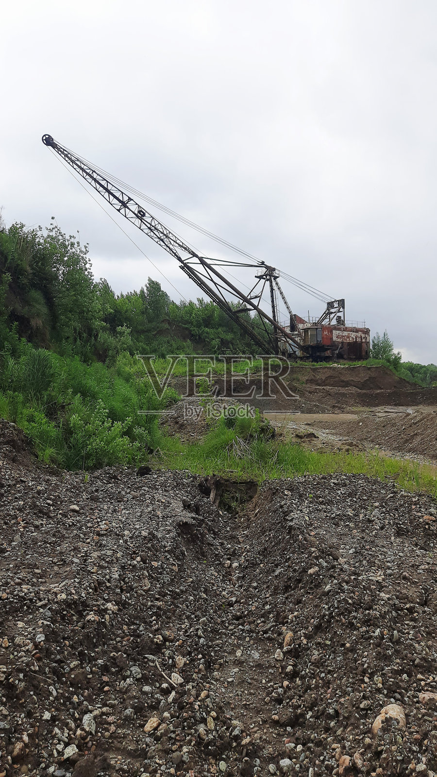 重型机械在绿树环绕的建筑工地上挖掘土壤，天空多云。照片摄影图片