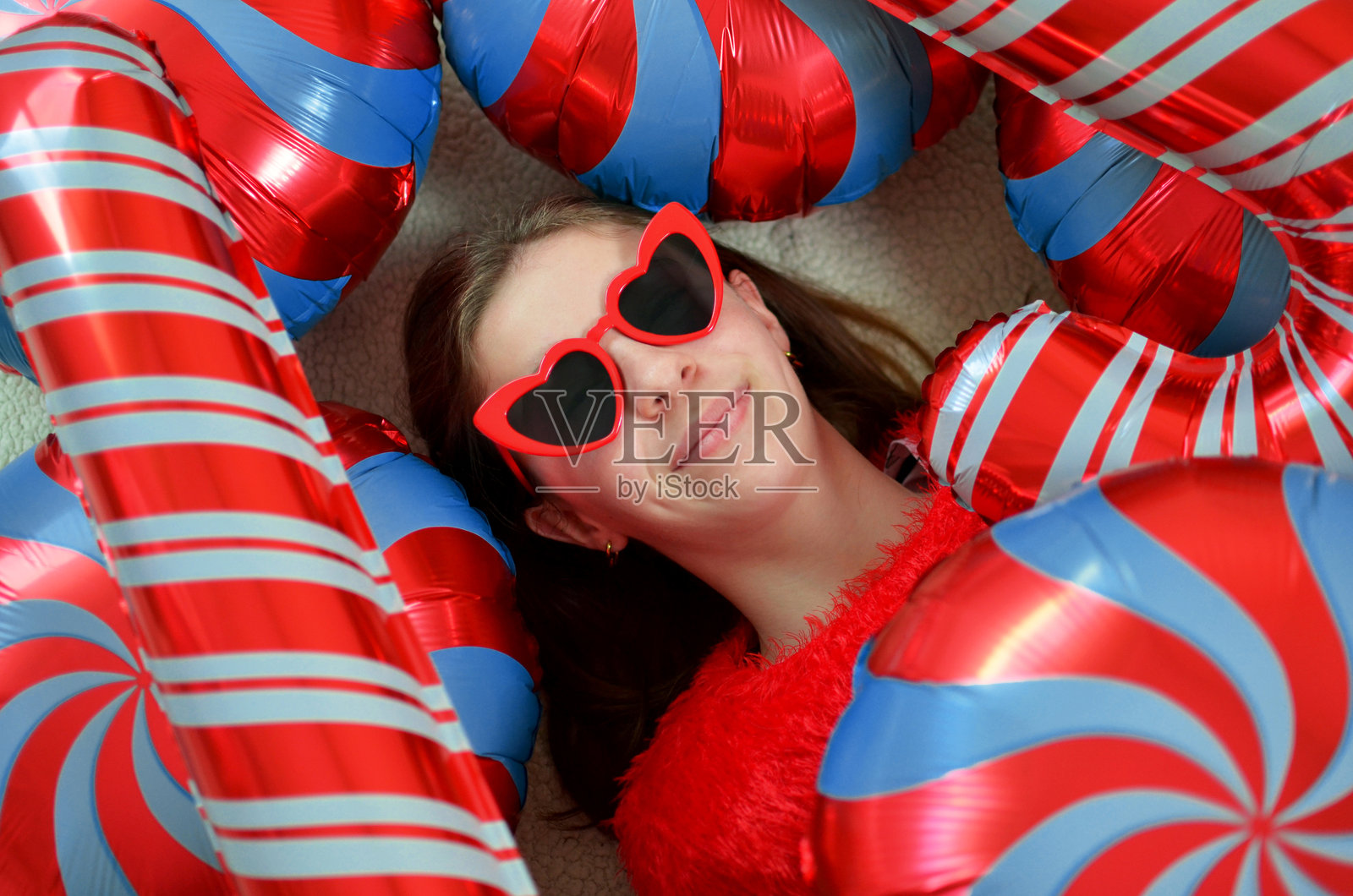 躺在圣诞糖果气球中，戴着心形太阳镜的少女照片摄影图片