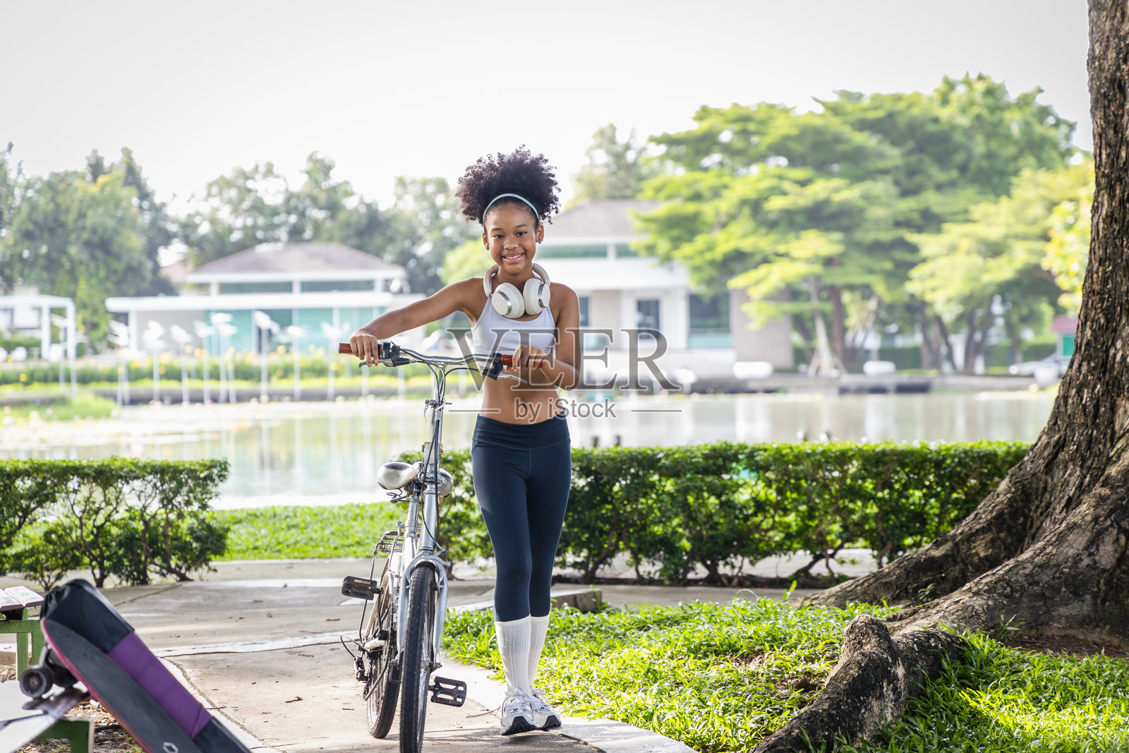 专注的非裔美国女孩戴着无线耳机在公园骑自行车，代表户外健身、骑行、健康生活方式和青少年健康。非常适合积极生活理念。照片摄影图片