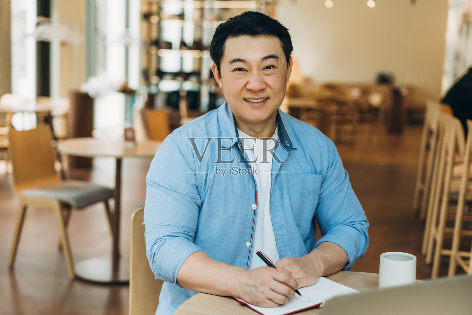 亚洲自由职业者在咖啡馆远程工作，正在笔记本上写笔记照片摄影图片