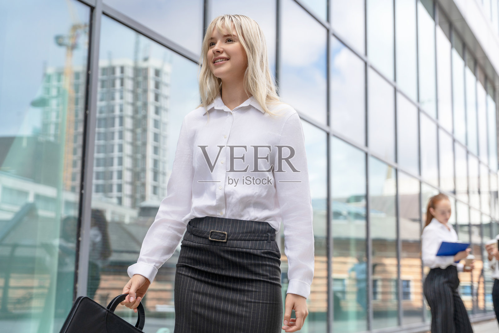 职业女性在现代城市环境中自信地走着，手提公文包，展现出专业与时尚。照片摄影图片