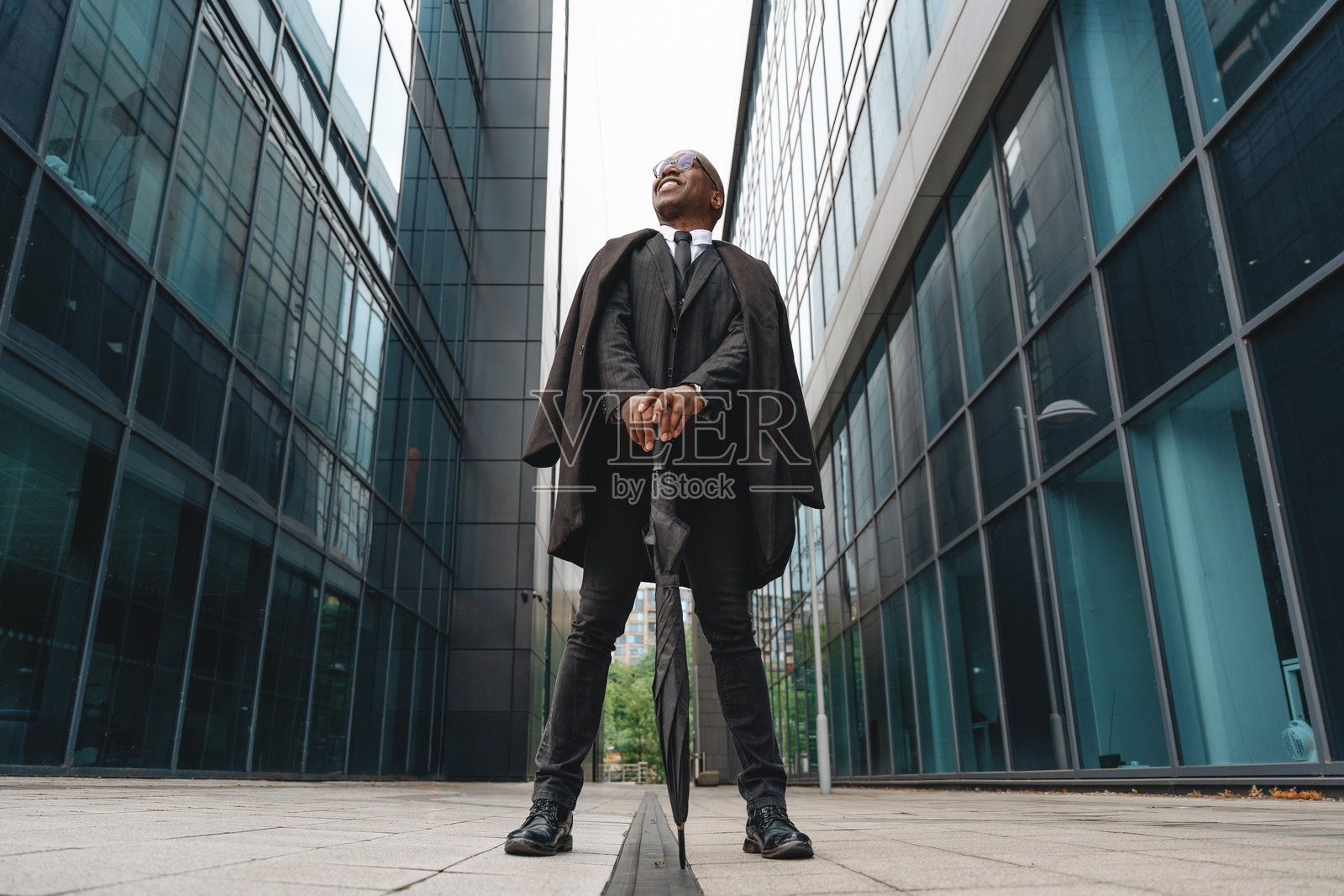 身穿正式服装的商人在城市环境中现代玻璃建筑之间自信地站立，白天的场景。照片摄影图片